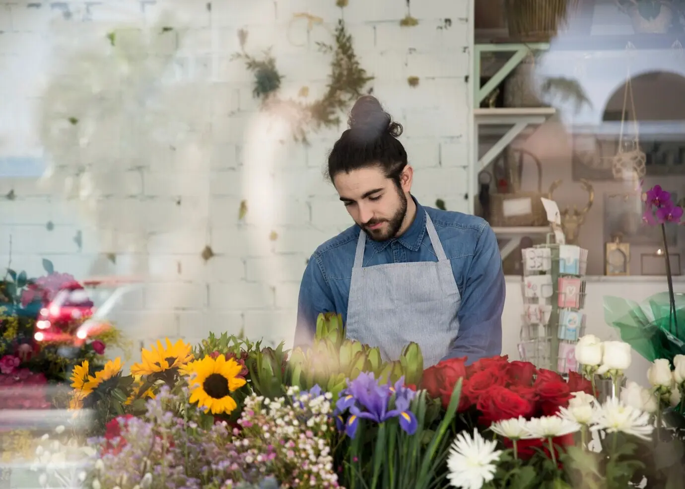 Porträt eines männlichen Floristen, der im Blumenladen hinter den bunten Blumen steht.